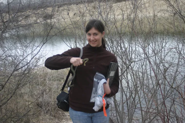 Paige holding a red-sided garter snake in the field, notebook and sample bags in hand